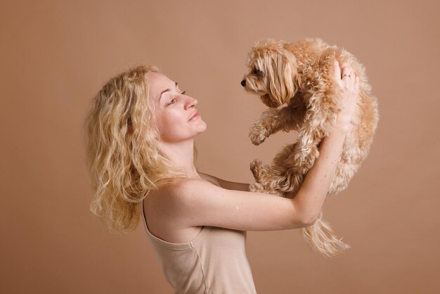 Foto una chica sostiene un lindo perro maltipoo en sus brazos primer plano en un fondo beige plano el concepto de amor por un perro