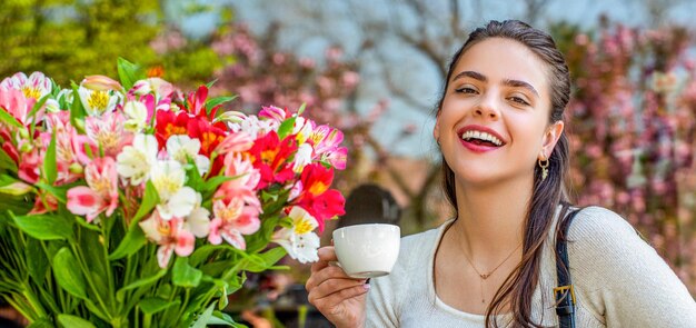 Chica sostiene una taza riendo flores de primavera mujer bebiendo café mujer de primavera moda