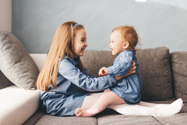 Chica con su hermanita divirtiéndose en el sofá Hermanos felices