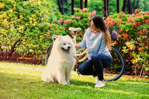 Una chica con su perro y una bicicleta al fondo de un parque.