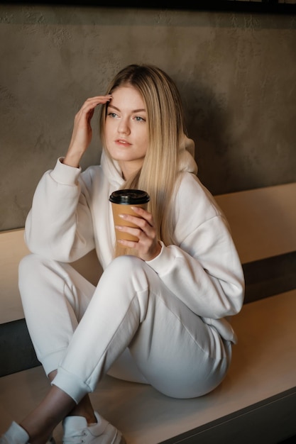 Chica con una sudadera con capucha blanca con café para llevar en la cafetería