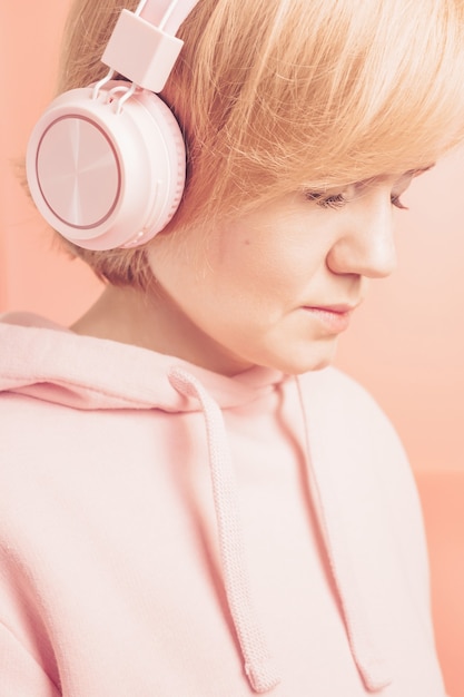 chica en una sudadera rosa y con auriculares rosas sobre un fondo similar en tono