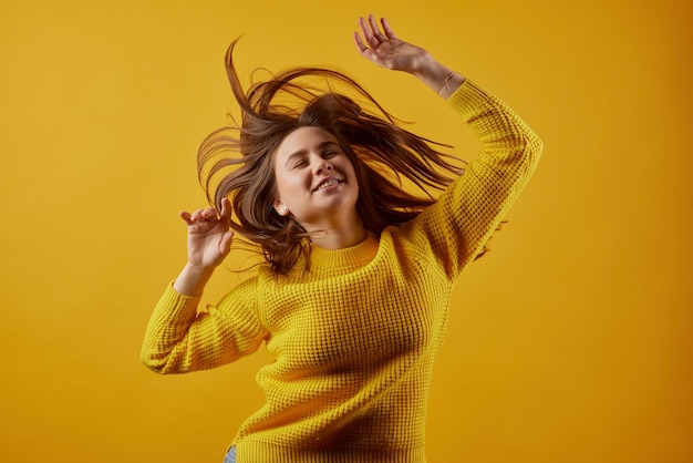 Chica en un suéter amarillo bailando sobre un fondo amarillo