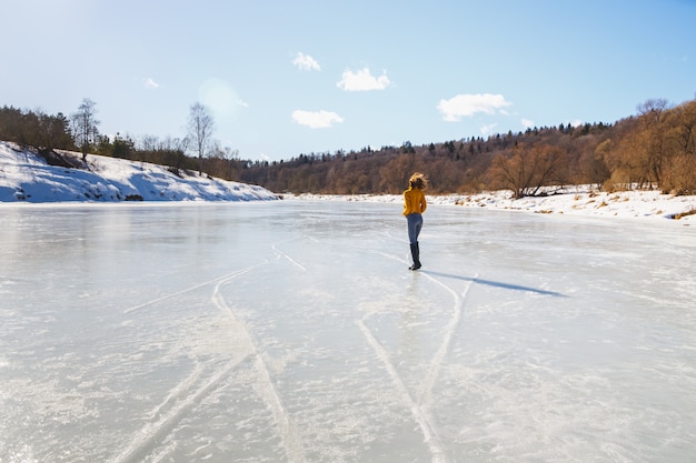 Chica en un suéter amarillo y corte de pelo corto en el hielo del río.