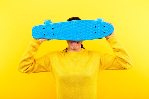 Chica con un suéter amarillo cubre su rostro con una patineta azul