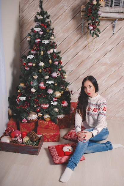 Chica en un suéter de Año Nuevo con el telón de fondo del árbol de Navidad