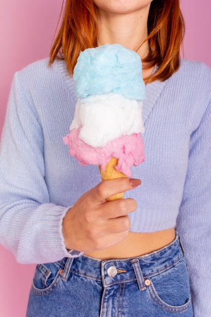 Chica con suéter azul y jeans y sosteniendo un helado de algodón de azúcar. Fondo rosa claro.