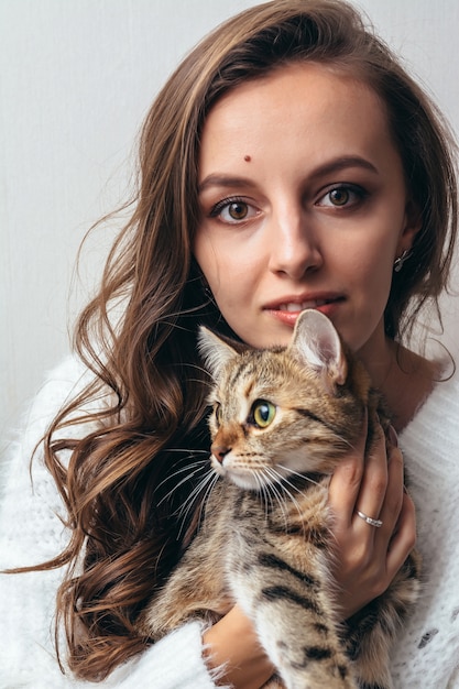 Chica en un suéter blanco abraza a un gato gris sobre un blanco