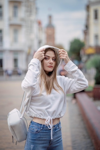 Foto una chica con un suéter blanco camina por la ciudad.