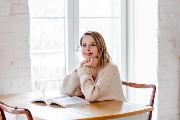 Chica en suéter blanco con libro sentado en la mesa