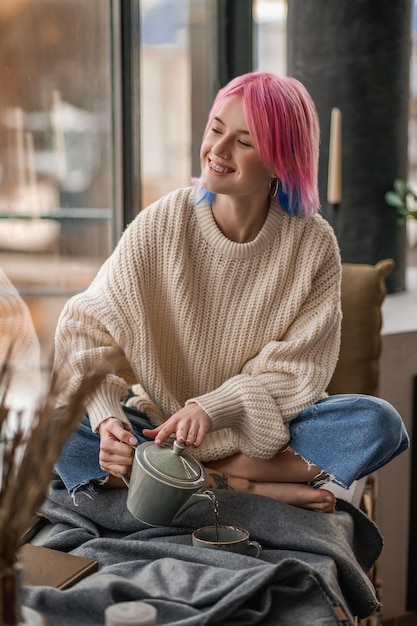 Una chica con un suéter blanco sirviendo té matutino en la taza.