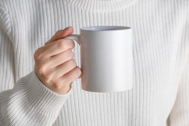 Chica en suéter blanco con taza de café de porcelana blanca maqueta de cerca