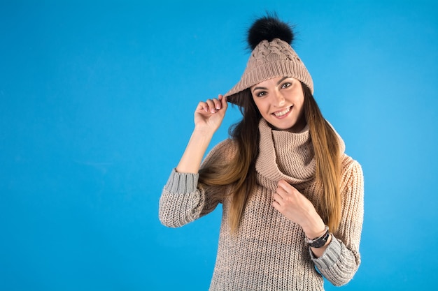 Foto chica en un suéter cálido, bufanda y sombrero sobre un fondo azul.