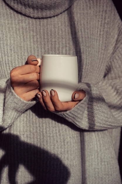 Una chica con un suéter cálido sosteniendo una taza en sus manos.