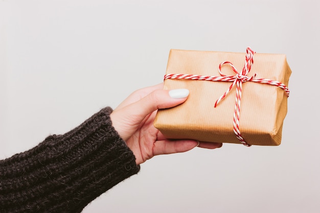 Chica en un suéter de lana negro sostiene un regalo de Navidad envuelto en papel, atado con una trenza