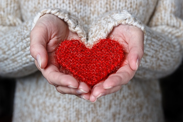 Chica con un suéter ligero da un corazón tejido.