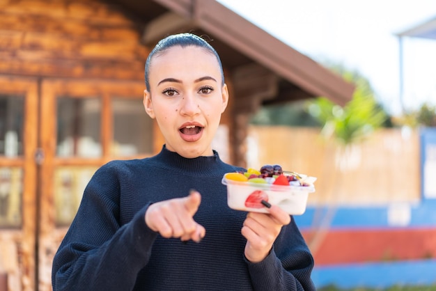 Una chica con un suéter negro sostiene un plato de fruta.
