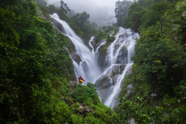 Foto la chica de suéter rojo recorriendo la cascada pi-tu-gro, hermosa cascada en la provincia de tak, thailand.