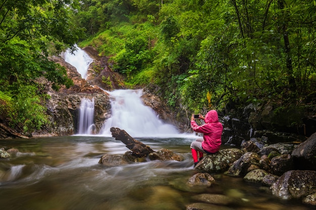 Foto la chica de suéter rojo recorriendo la cascada pi-tu-gro, hermosa cascada en la provincia de tak, thailand.