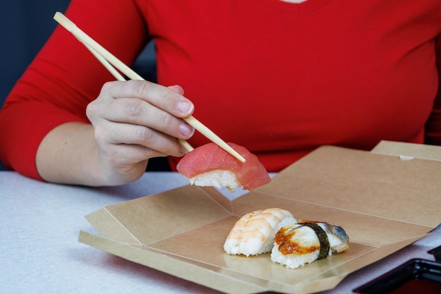 Una chica con un suéter rojo sostiene sushi de atún con palillos