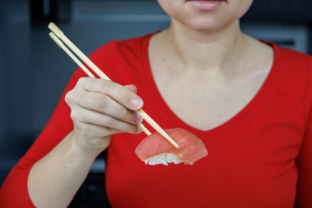 Una chica con un suéter rojo sostiene sushi de atún con palillos