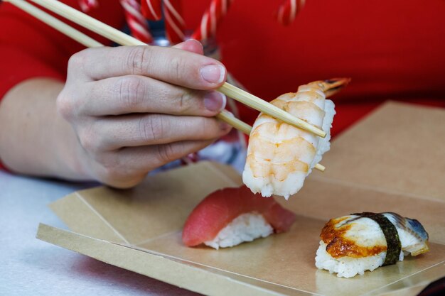 Una chica con un suéter rojo sostiene sushi con langostinos con palillos