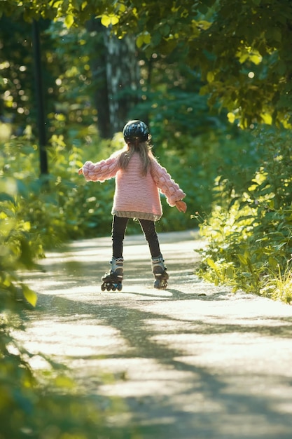 Una chica con suéter rosa patinando en el bosque sobre sus ruedas.