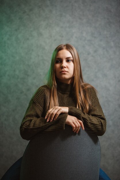 Chica en un suéter verde y jeans en una silla gris y sonriendo