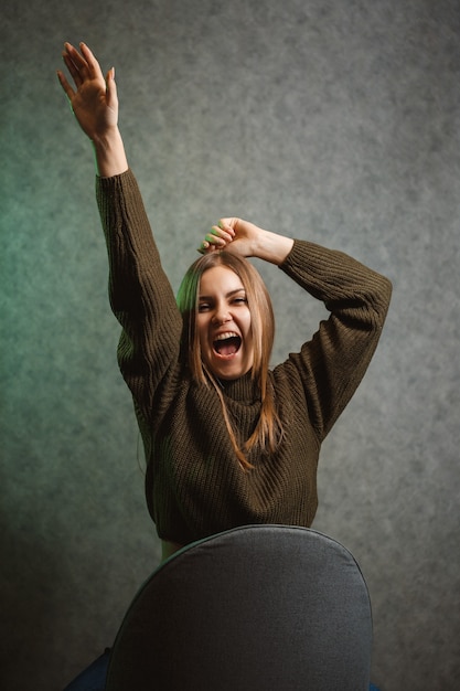 Foto chica en un suéter verde y jeans en una silla gris y sonriendo