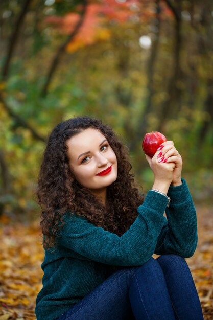 Chica con un suéter verde y una manzana en sus manos en el bosque de otoño
