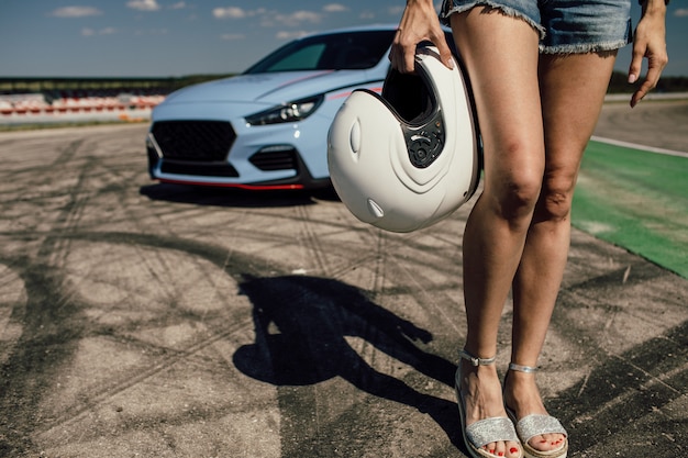 Chica sujetando un casco junto a un auto deportivo