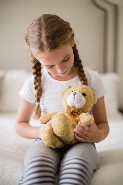 Chica sujetando un oso de peluche en la cama en el dormitorio