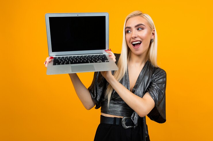 Foto chica sujetando portátil con pantalla en blanco para la página web sobre fondo amarillo