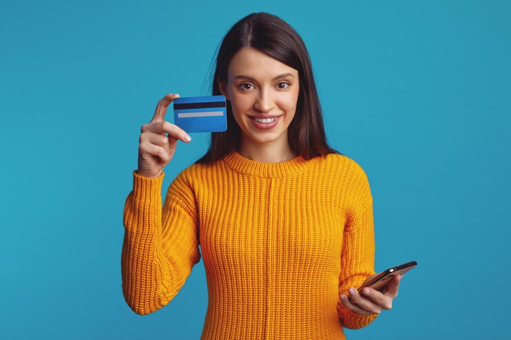 Chica sujetando smartphone y tarjeta de crédito de plástico aislado sobre fondo azul.