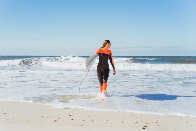 chica de surf en la costa del océano en un traje de neopreno con tabla de surf