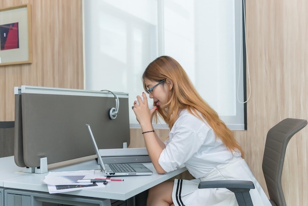 Chica tailandesa trabaja en el escritorio empresaria con vestido blanco que trabaja en la empresa bebe café entre el trabajo