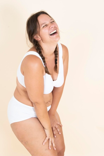 Chica de talla grande en lencería con dos trenzas sonriendo y mostrando su cuerpo orgullosa de su cuerpo