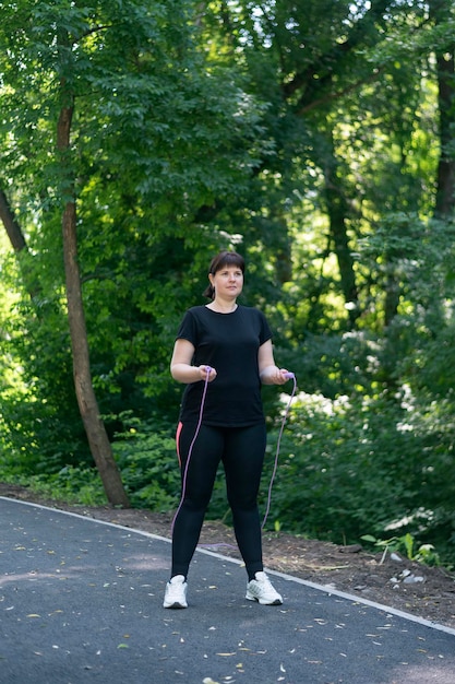 Chica de talla grande de pie con una cuerda en sus manos en un parque de verano. Trenes de mujer joven con sobrepeso en el parque. Marco vertical.