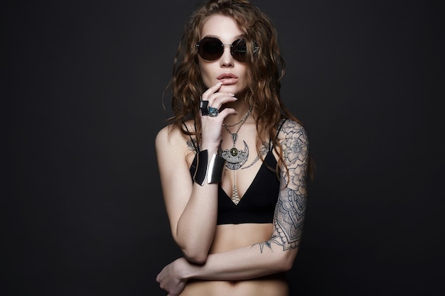 Chica tatuada en ropa interior, gafas de sol y joyas.