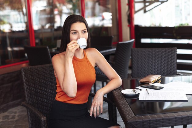 Chica con una taza de café sentado en un café. Amplia sonrisa. Hermosa piel limpia. Mujer de negocios después de firmar documentos. Reunión de negocios.