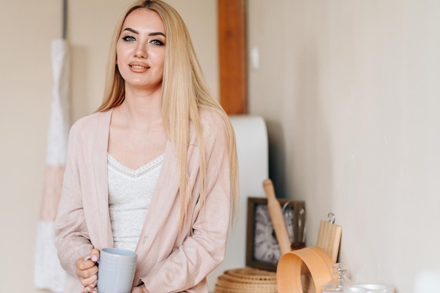 Chica con taza en ropa de casa está de pie en la cocina Retrato de primer plano de la joven amante