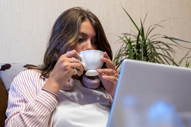 Chica con una taza de té en la mano está escribiendo en una computadora portátil