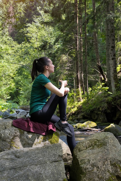 Chica con una taza de té sentado en una roca en el bosque. Día de verano