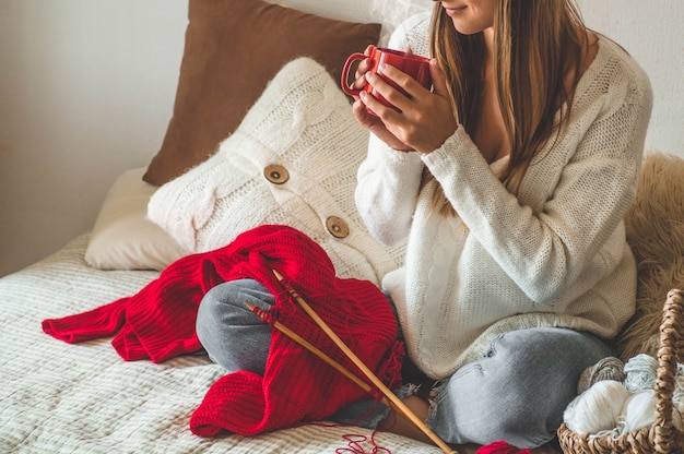 Chica teje un suéter caliente con una taza de té caliente en la cama