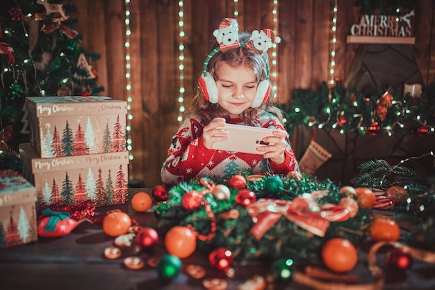 Chica con teléfono cerca del árbol de Navidad en el interior decorativo.