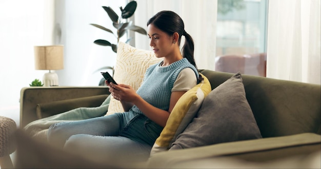 Chica teléfono y escribir en casa en el sofá para la comunicación relajarse y aplicación móvil con rollo de redes sociales Mujer teléfono inteligente y mensajes de texto en la sala de estar para correo electrónico de Internet o bienestar con transmisión
