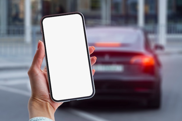 Chica tiene un teléfono inteligente en sus manos. Simulacros de teléfono con pantalla blanca en el fondo del coche.