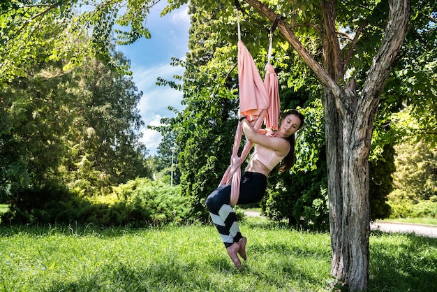 Una chica con un tipo de figura delgada decidió practicar ejercicios de yoga al aire libre cuando hace buen tiempo Concepto de mosca de yoga al aire libre en el árbol