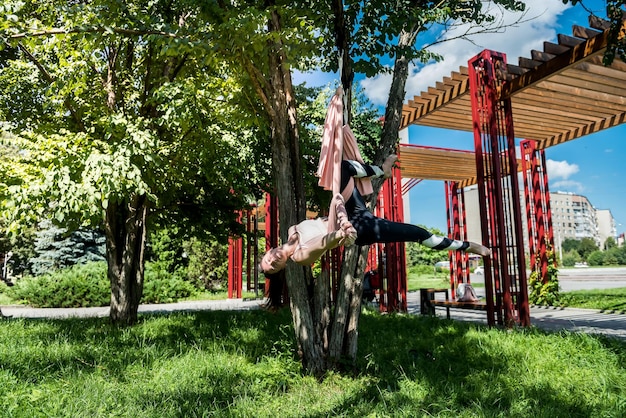 Una chica con un tipo de figura delgada decidió practicar ejercicios de yoga al aire libre cuando hace buen tiempo Concepto de mosca de yoga al aire libre en el árbol