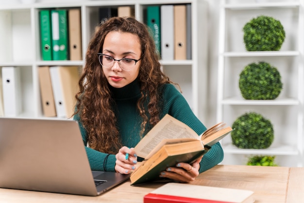 Chica de tiro medio estudiando con diccionario y computadora portátil